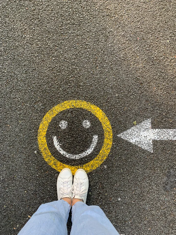 Woman looking down at her sneakers on the street standing on a smiley face