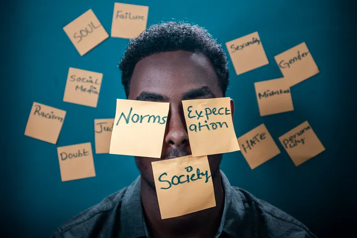 Man with post-its on his face reading norms, expectation, and society