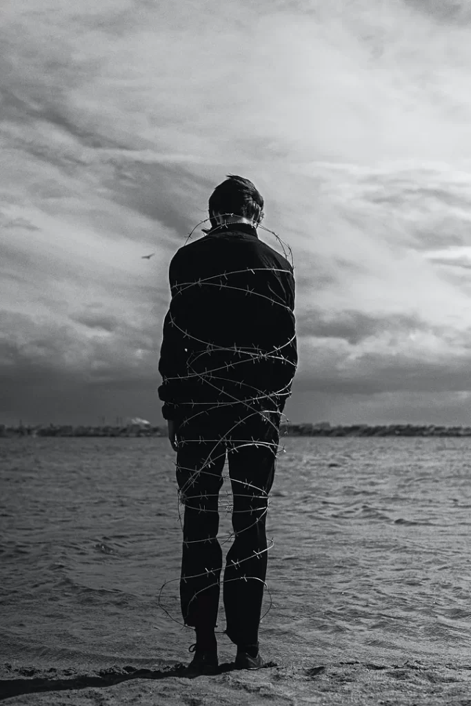 The back of a man bound by barbed wire at the edge of the ocean