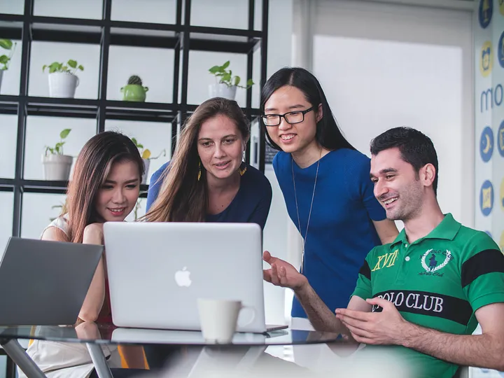 Four intrigued and happy people looking over a laptop