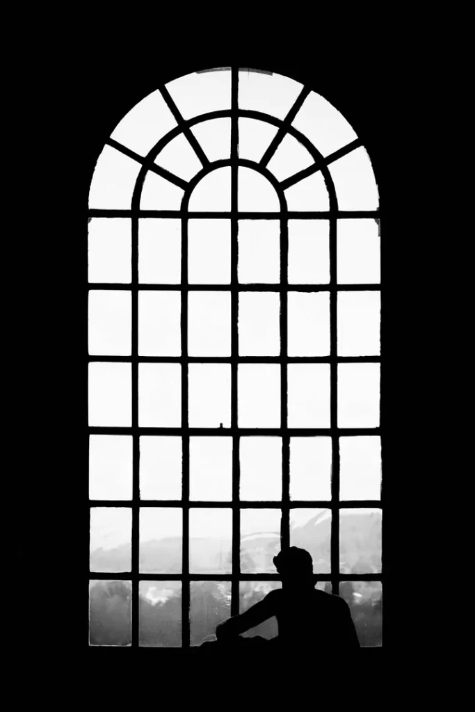 A man in silhouette before a large, arched window.