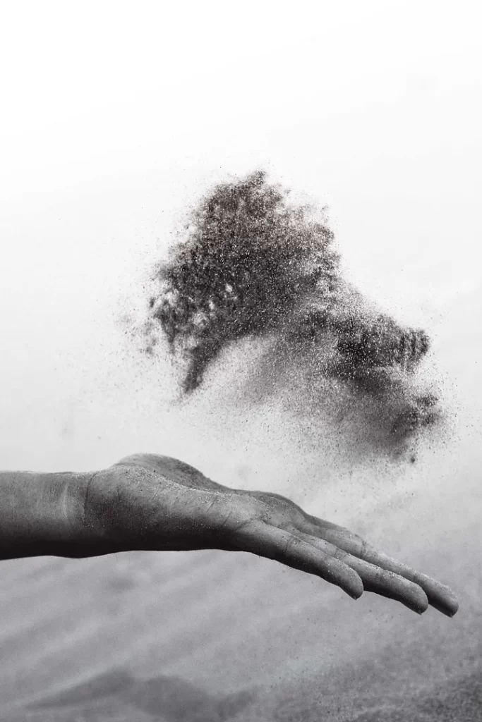 Black and white close up of a hand tossing sand.