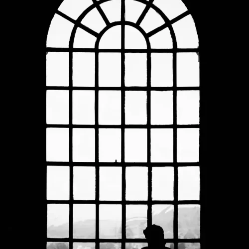 A man in silhouette before a large, arched window.